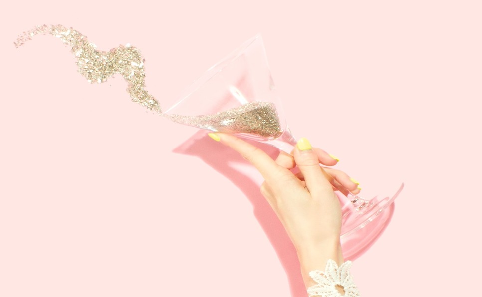 A woman's hand throwing gold glitter champagne on a pink background