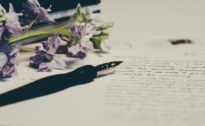 A fountain pen writing with some purple flowers