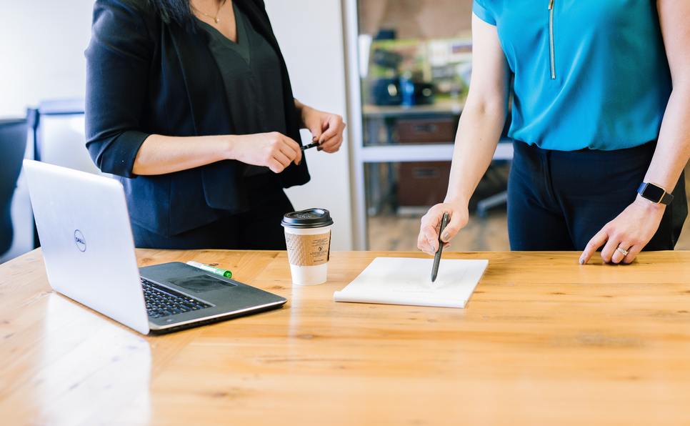 Two people signing a contract on a desk with a laptop