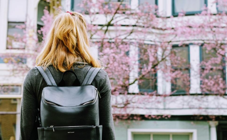 Woman with backpack outside school showing why you need an MFA in Creative Writing