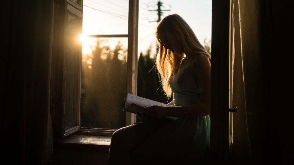 Woman in shadow sitting on windowsill reading books with unreliable narrators